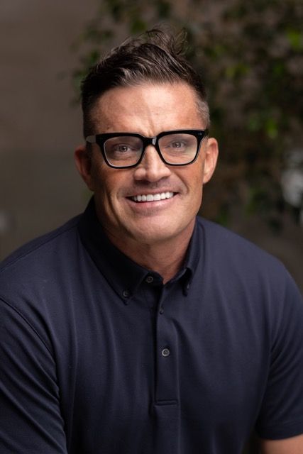 A man wearing glasses and a blue shirt is smiling for the camera.