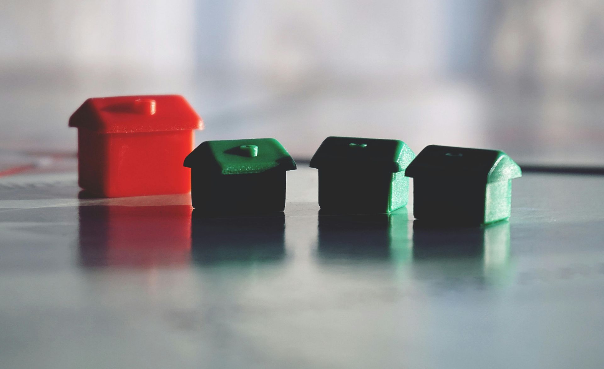 Four small house-shaped blocks on a reflective surface, including one red and three dark green
