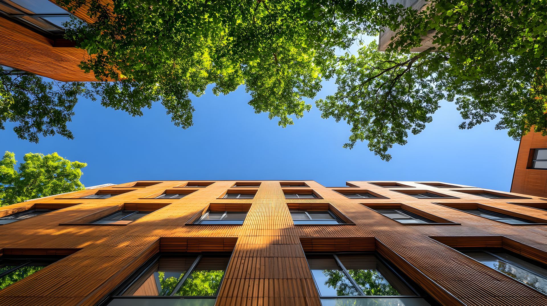 Maison moderne à deux étages avec des éléments en bois, de grandes fenêtres et une cheminée, située dans un quartier boisé avec pelouse.