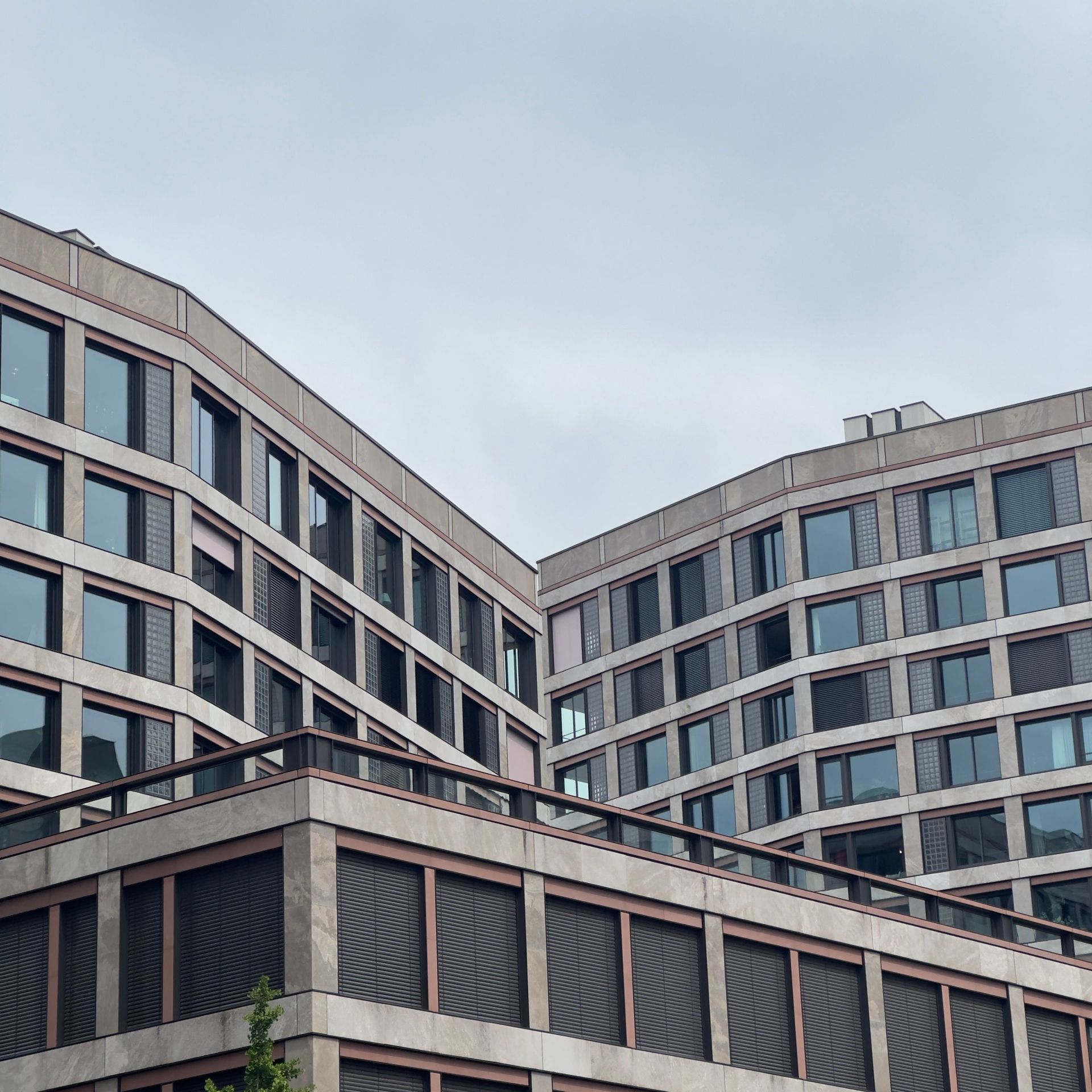 Immeubles de bureaux modernes aux formes courbes, avec des façades grises et des rangées de fenêtres se détachant sur un ciel nuageux.