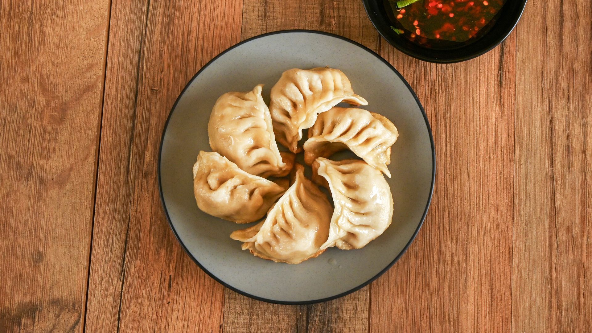 Plate of steamed dumplings on a wooden table with a small bowl of dipping sauce