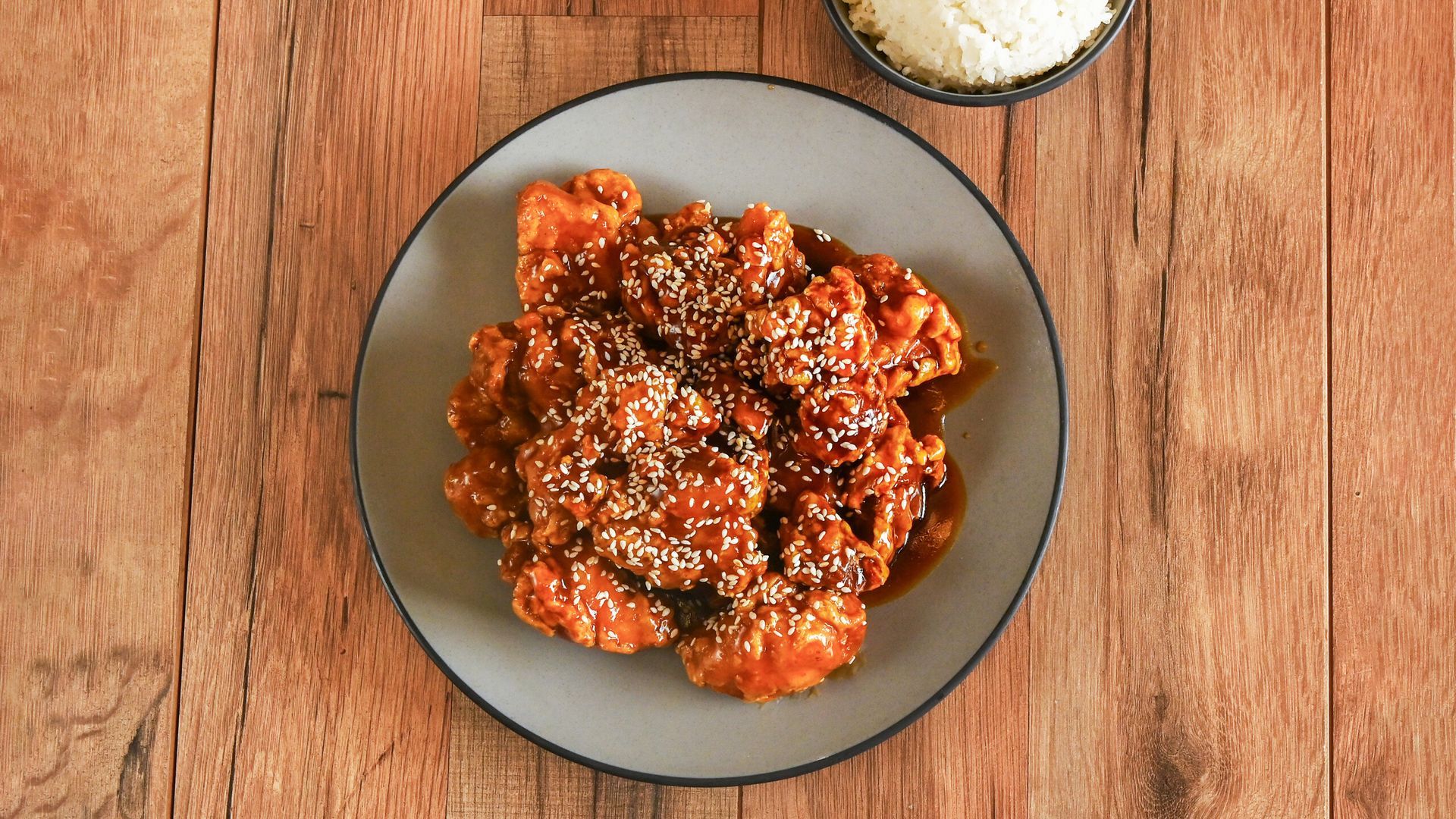 Plate of saucy chicken wings topped with sesame seeds on a wooden table