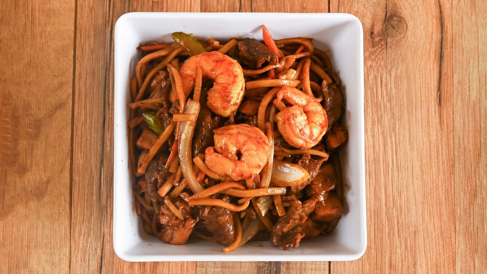 Shrimp and noodles in a white square bowl on a wooden table