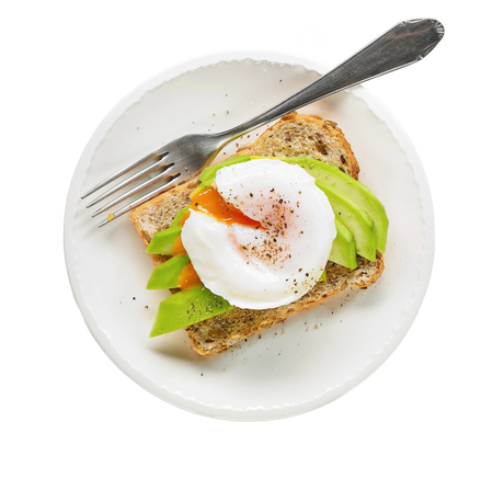 Toast con uovo in camicia e avocado su un piatto bianco con forchetta