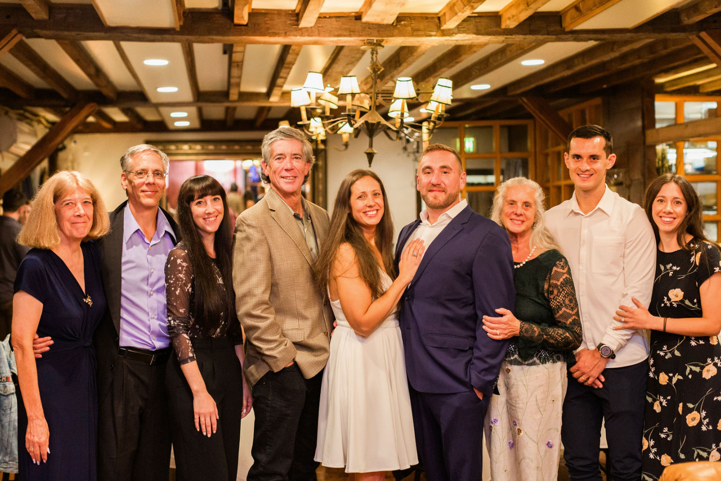 9 people stading together, all smiling in a beautiful room with wood beams and lighting
