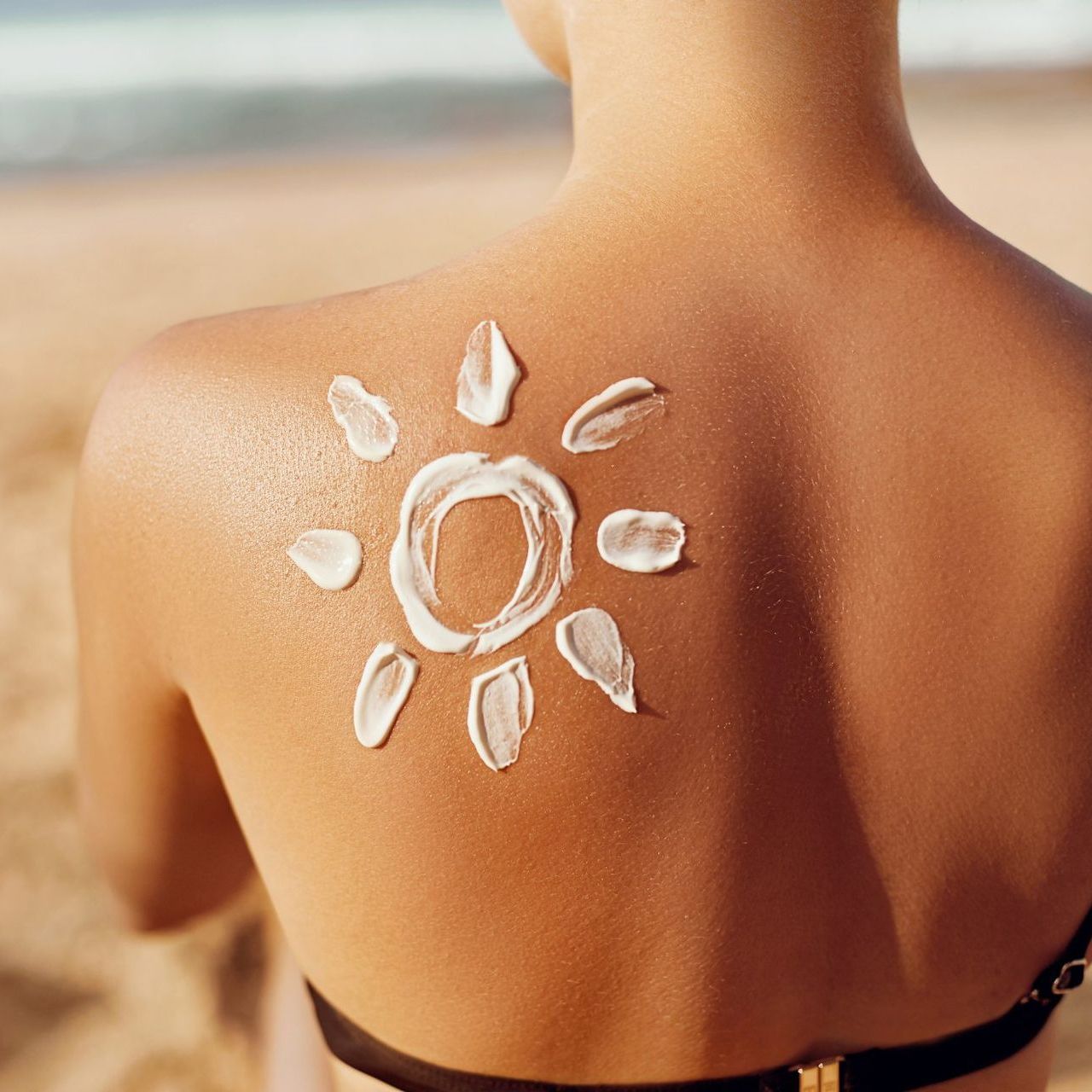 A woman is sitting on the beach with sunscreen on her back.