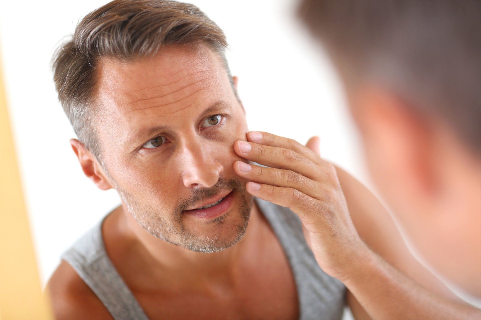 man with forehead wrinkles touching face looking in the mirror