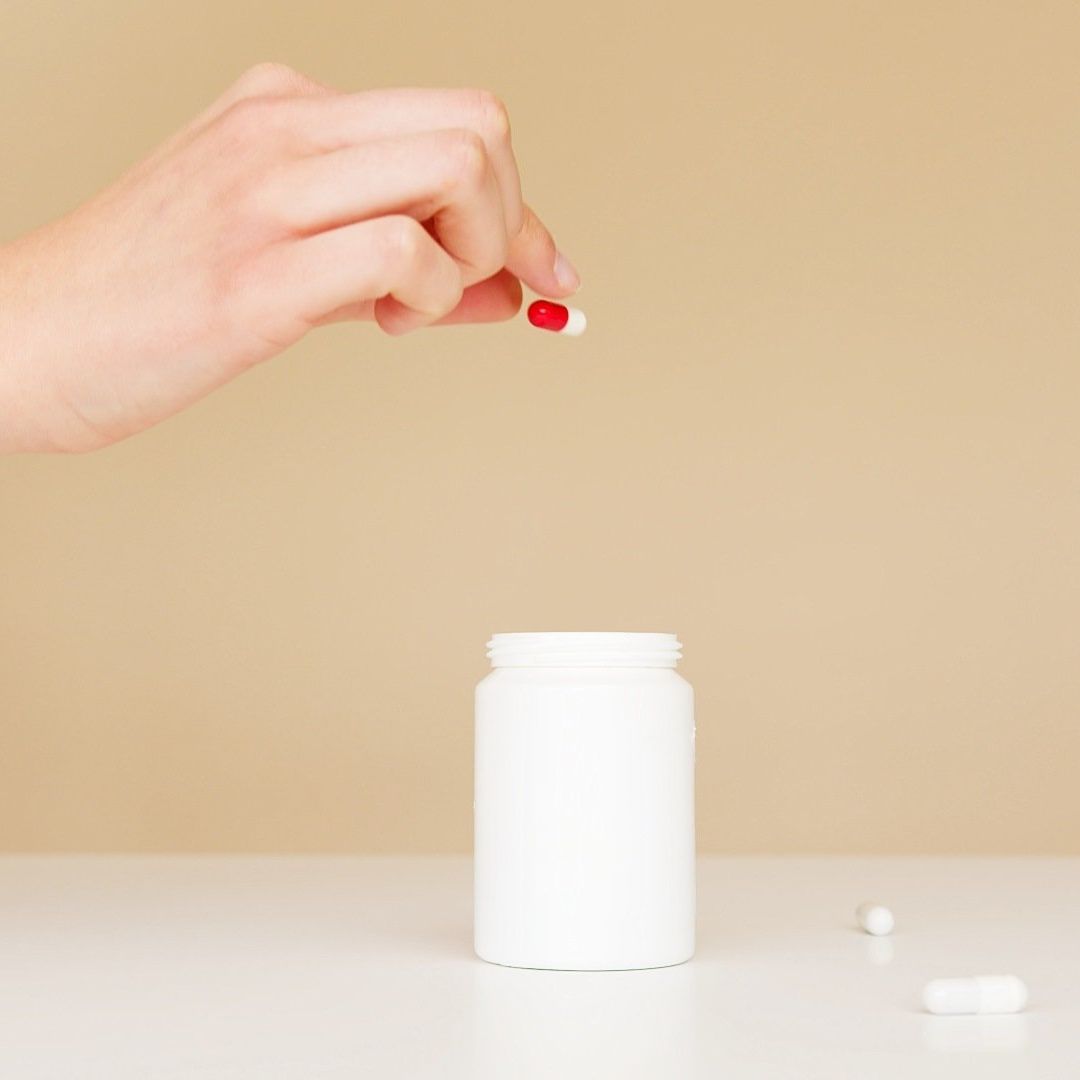 A person is taking a red pill out of a white bottle.
