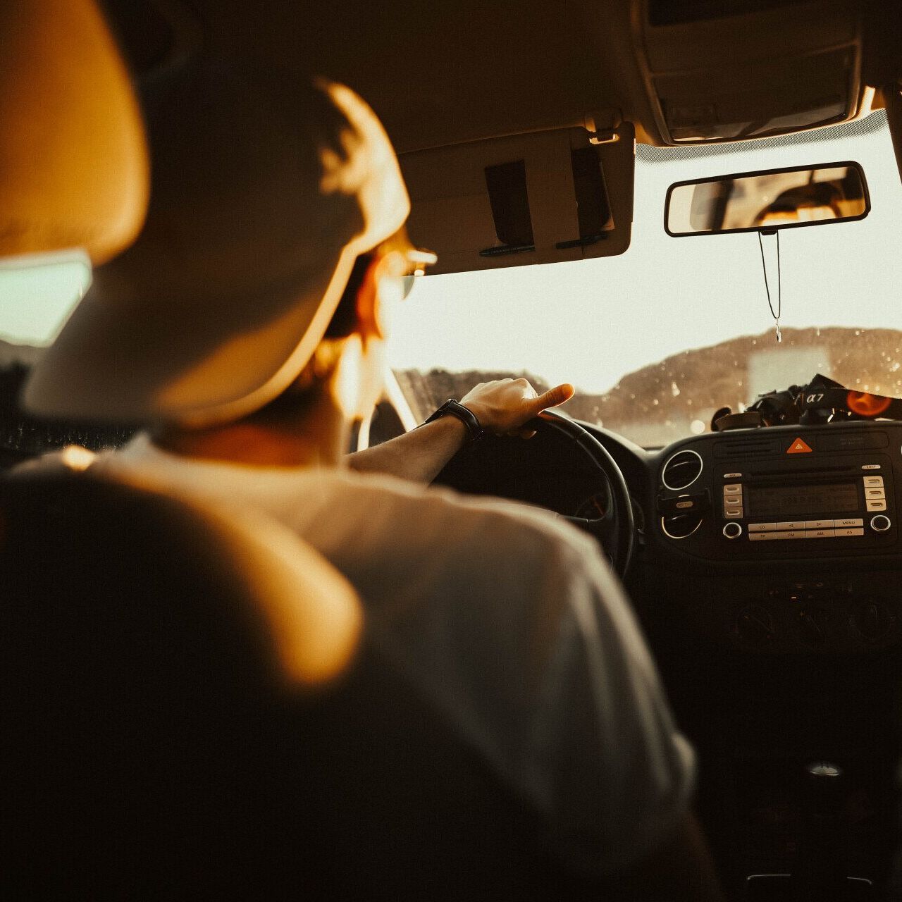 A man is driving a car with another man in the back seat.