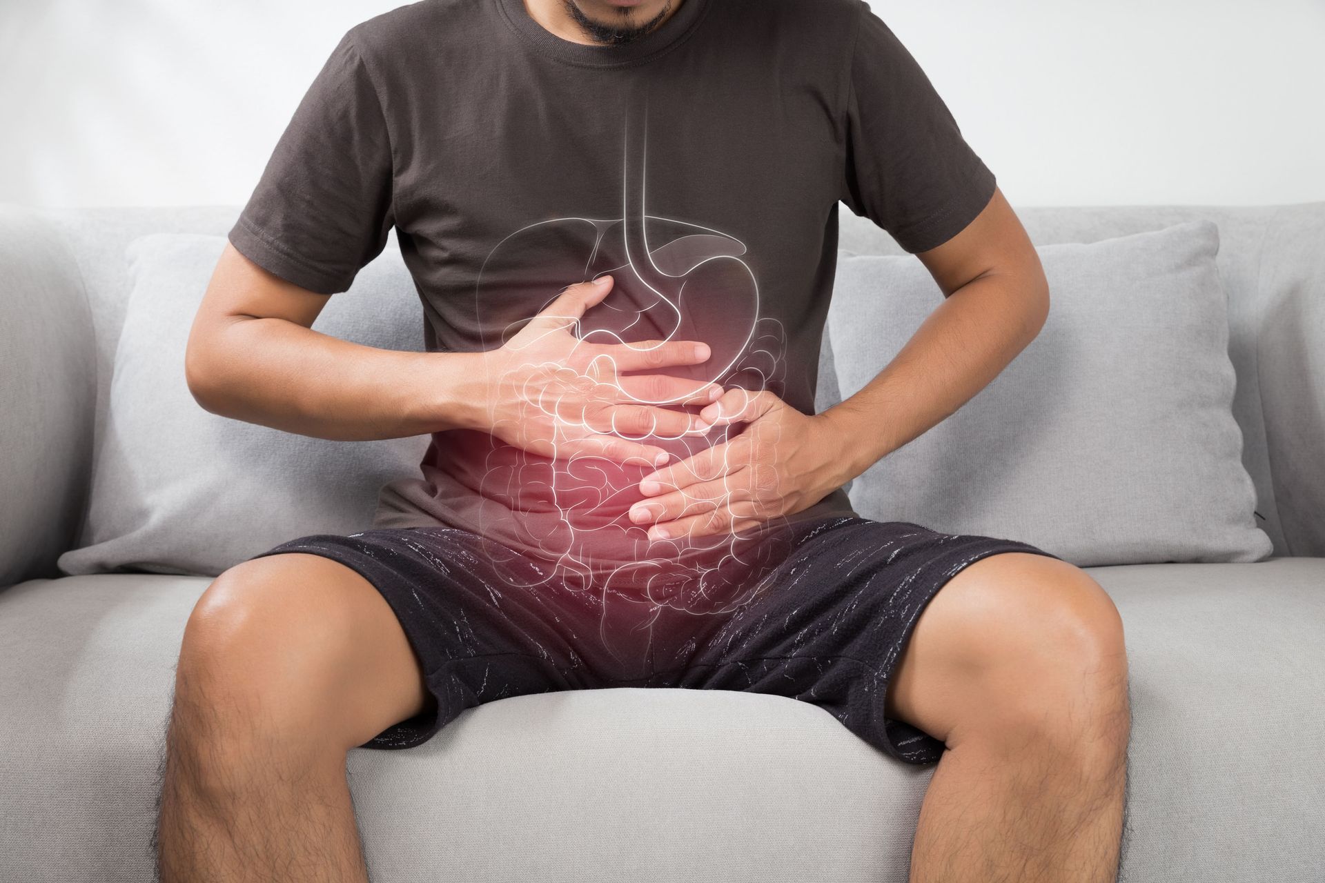 Pessoa sentada em um sofá, segurando a barriga, com uma imagem de dor intensa sobreposta ao abdômen.