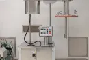Stainless steel laboratory mixing machine with a control panel, vertical shaft, and gauge mounted against a white wall.