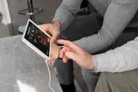 Two people sit together, one holding a white smart home display while the other points to the touchscreen interface.