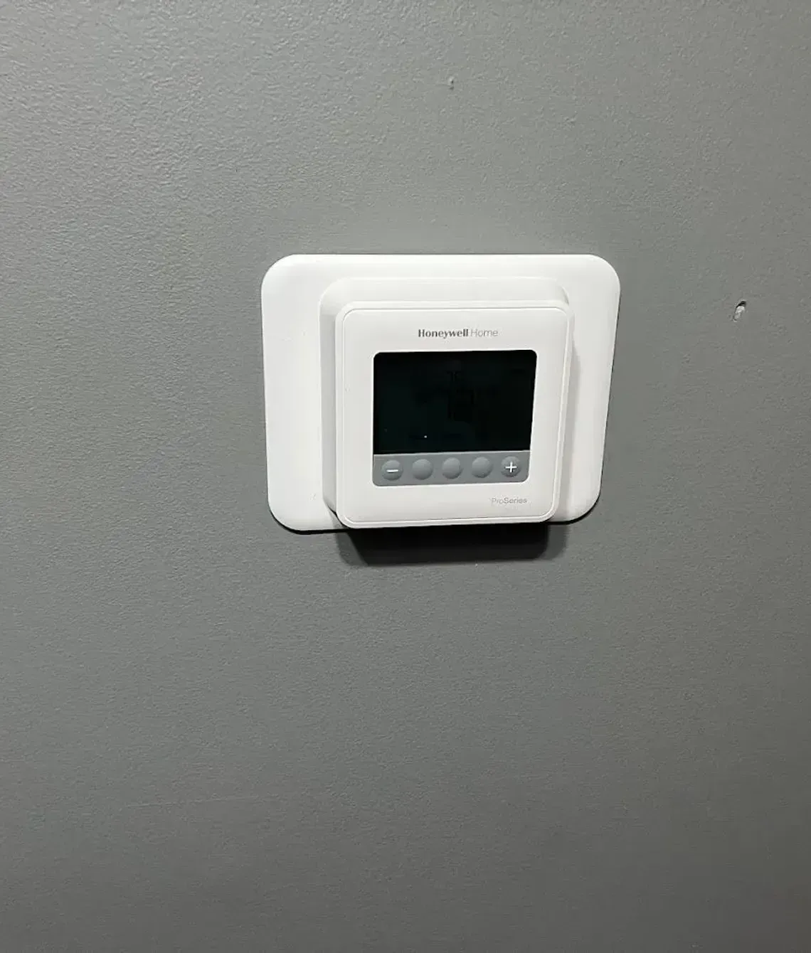 A white digital wall thermostat mounted on a grey wall.