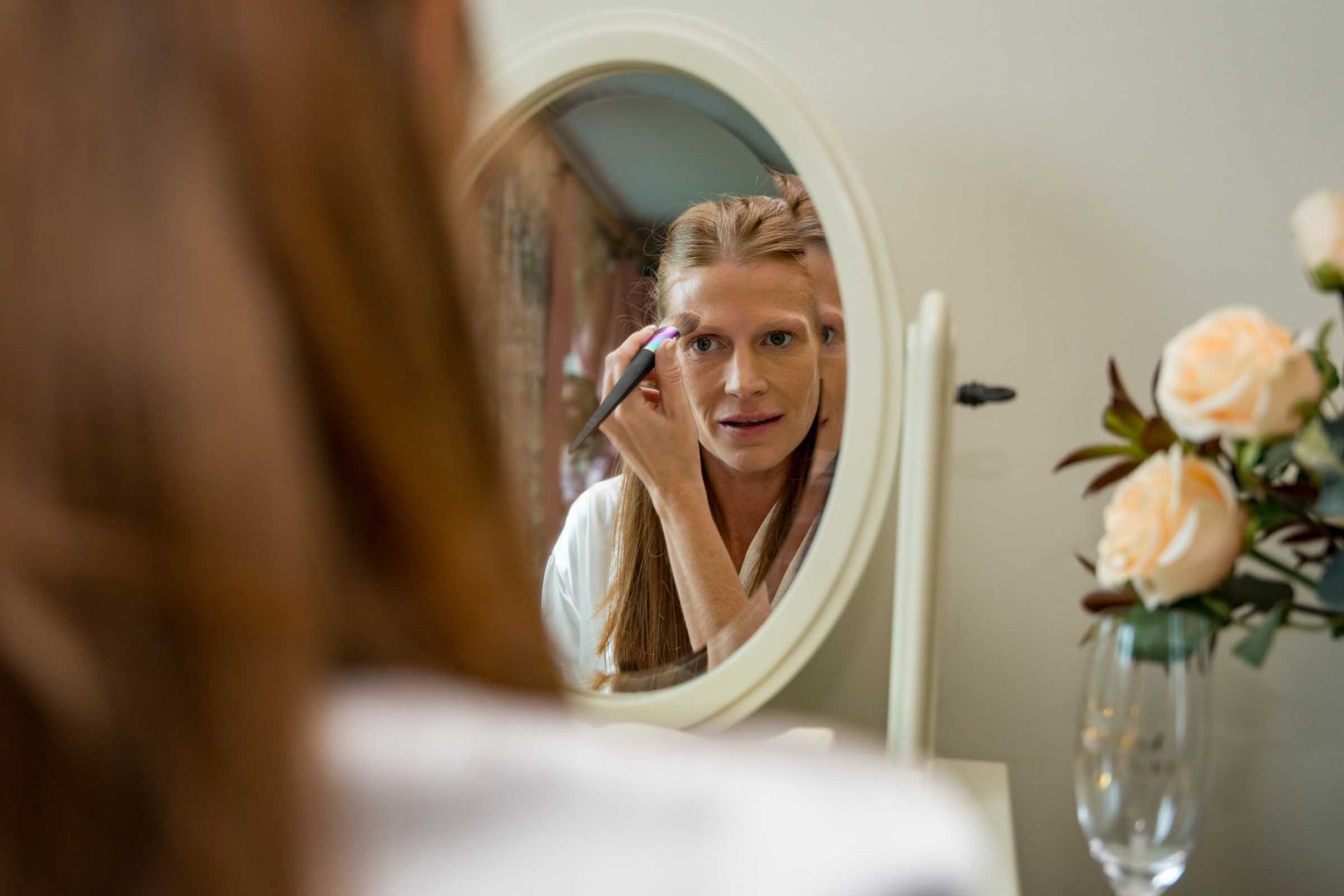 A woman is applying makeup in front of a mirror.