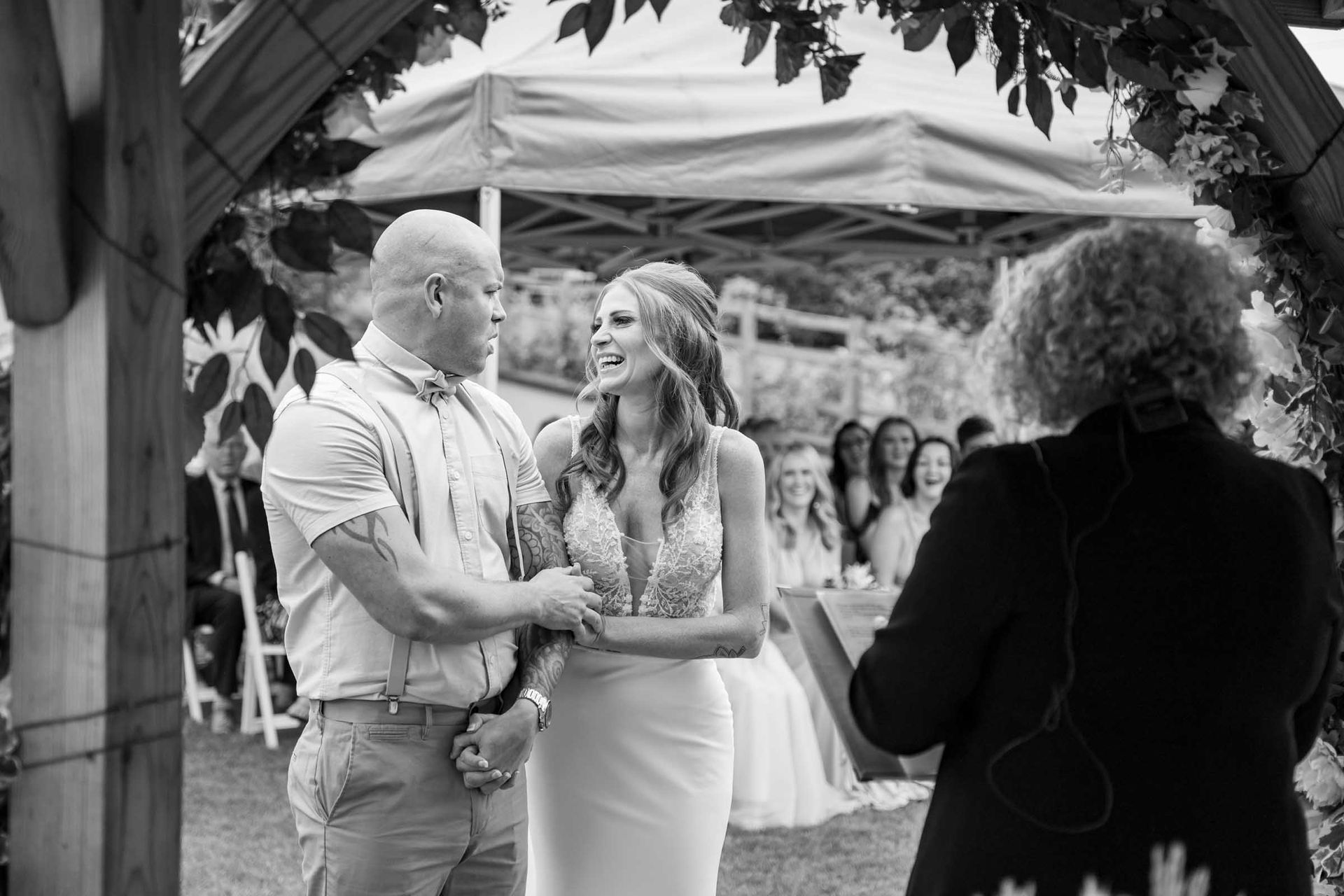 A black and white photo of a bride and groom holding hands during their wedding ceremony.