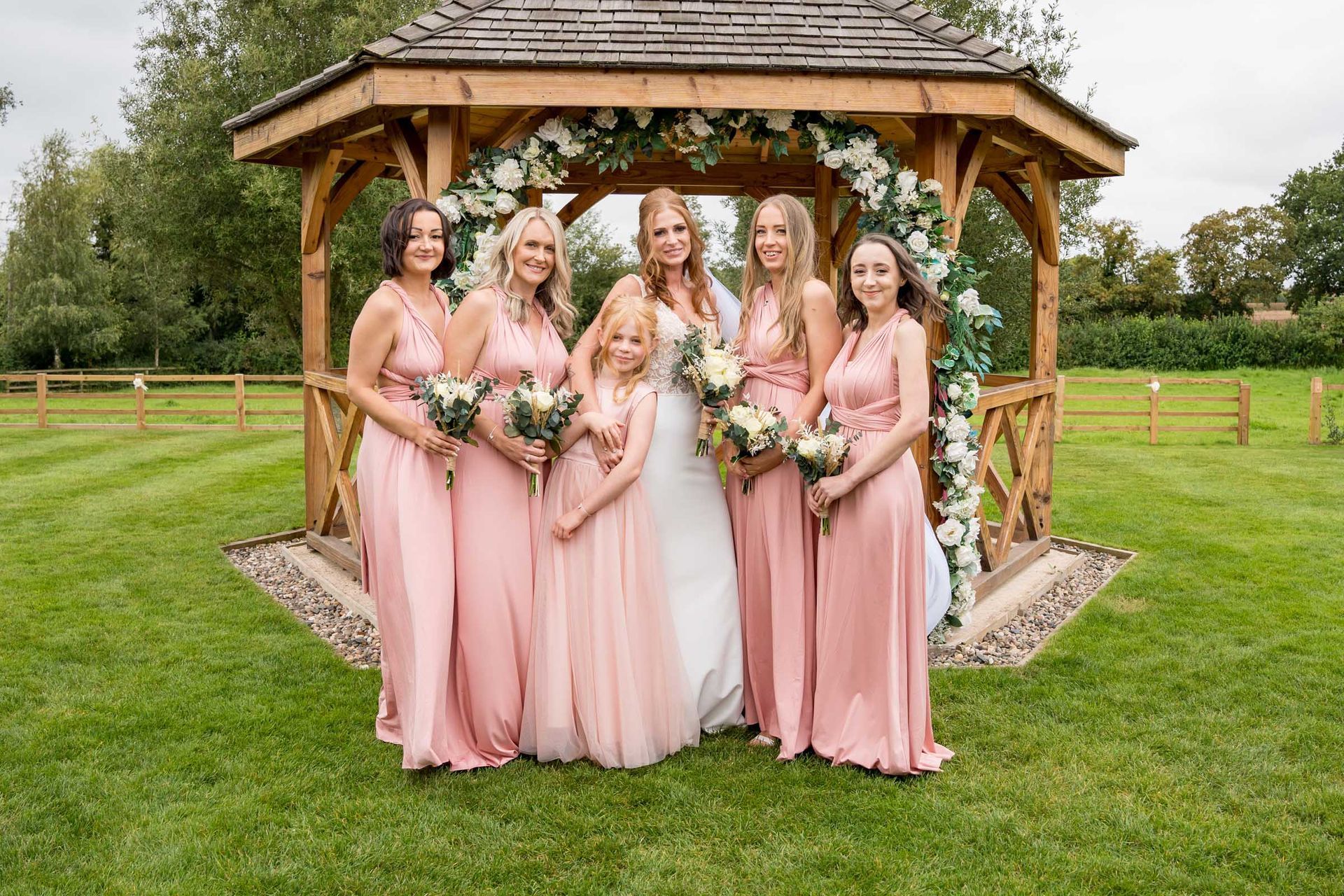 A bride and her bridesmaids are posing for a picture in front of a gazebo.