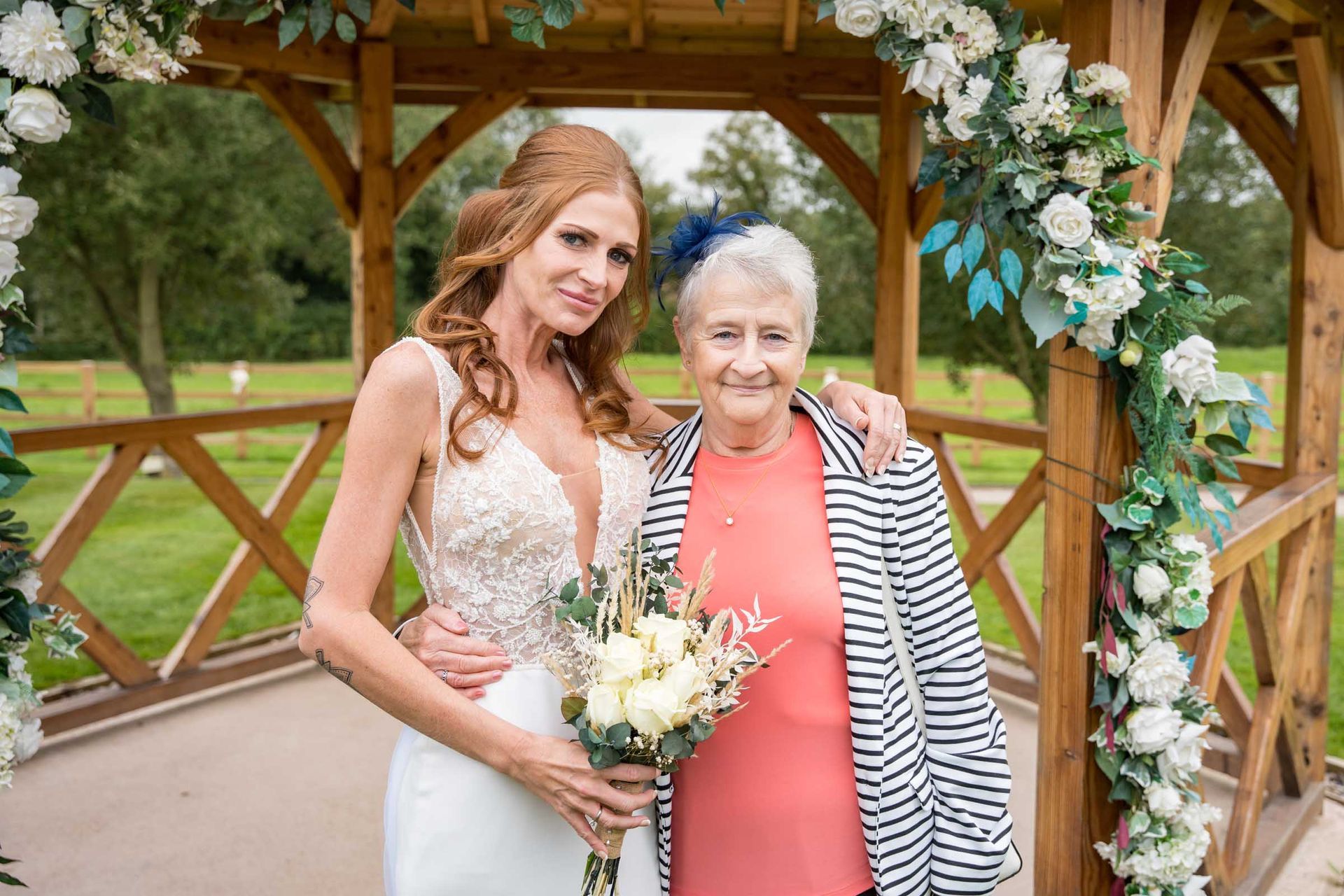 A bride and her grandmother are posing for a picture in front of a gazebo.