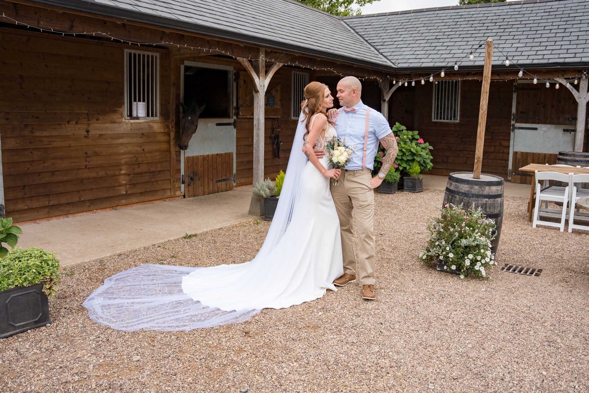 A bride and groom are posing for a picture in front of a horse stable.