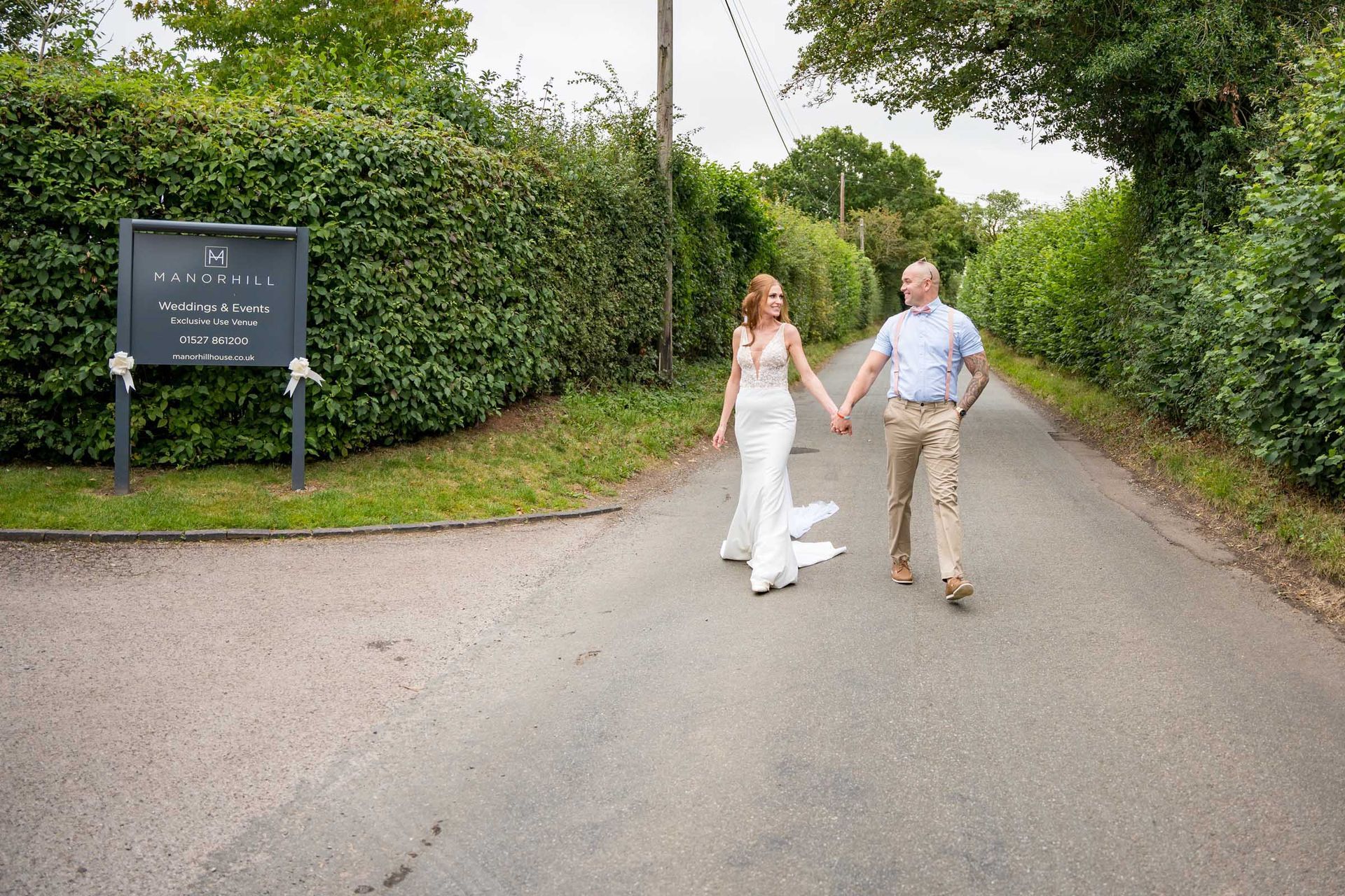 A bride and groom are walking down a road holding hands.