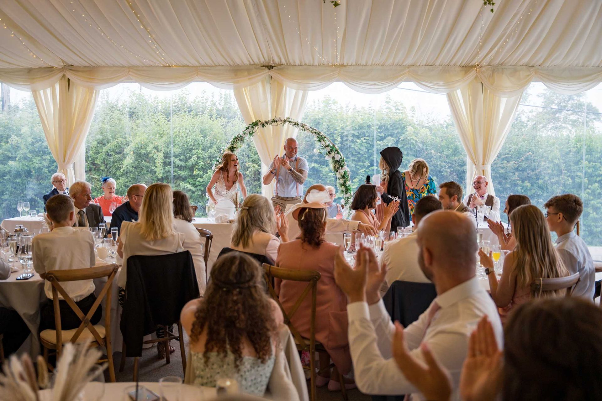 A group of people are sitting at tables in a tent at a wedding reception.