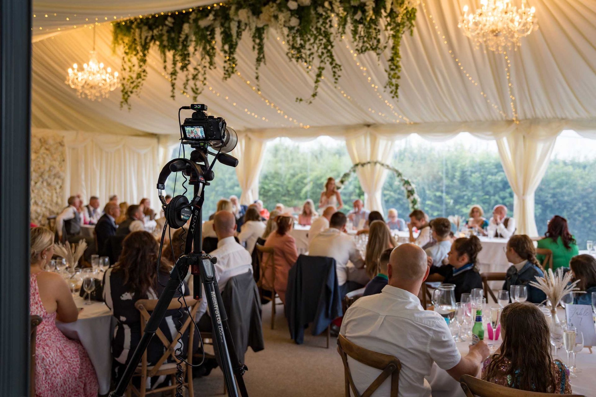 A group of people are sitting at tables in a tent at a wedding reception.
