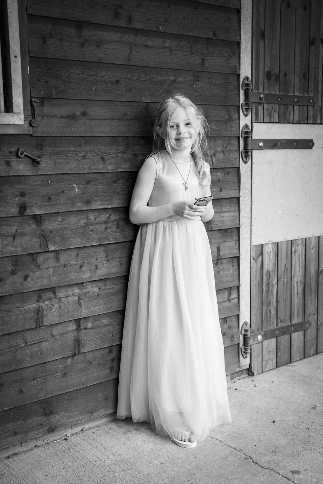 A young girl in a white dress is leaning against a wooden wall.