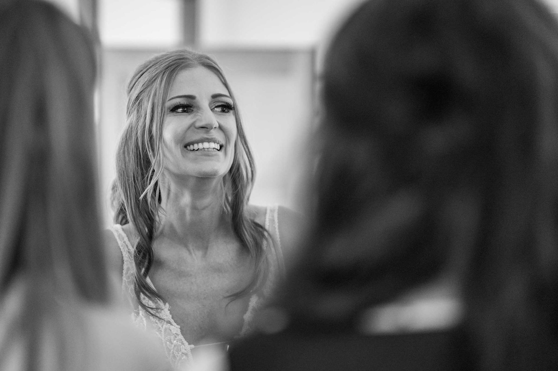 A black and white photo of a woman smiling in front of a mirror.