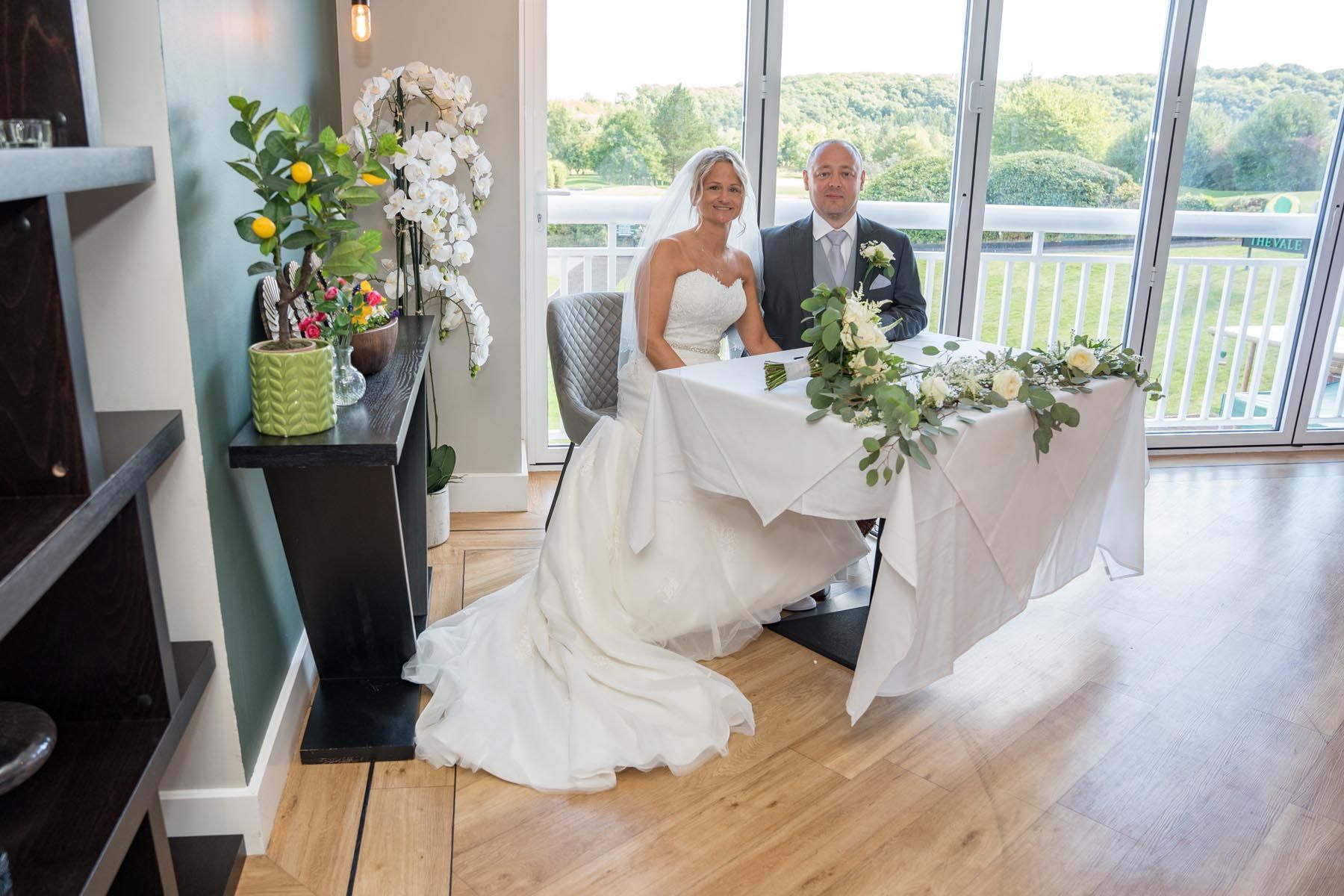 A bride and groom are sitting at a table in front of a window.