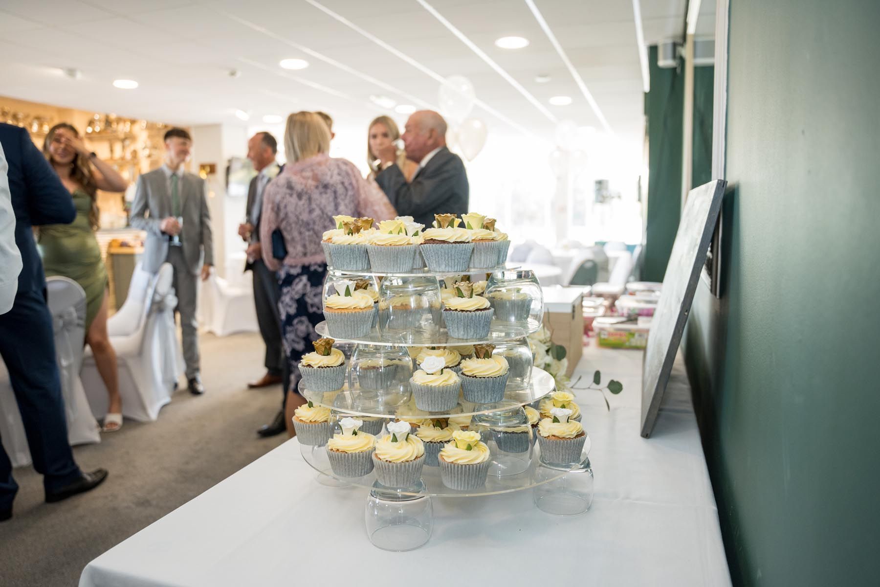 A group of people are standing around a table with cupcakes on it.