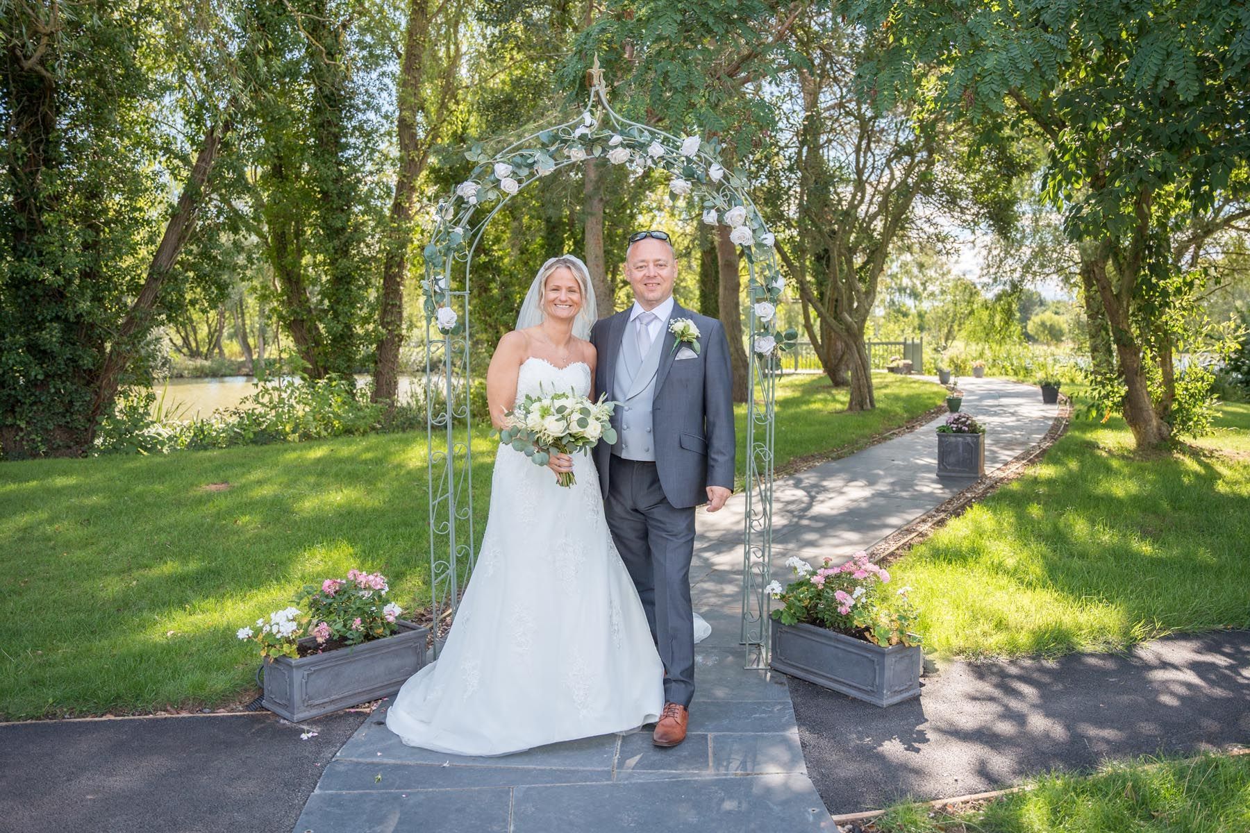 A bride and groom are standing next to each other on a path in a park.