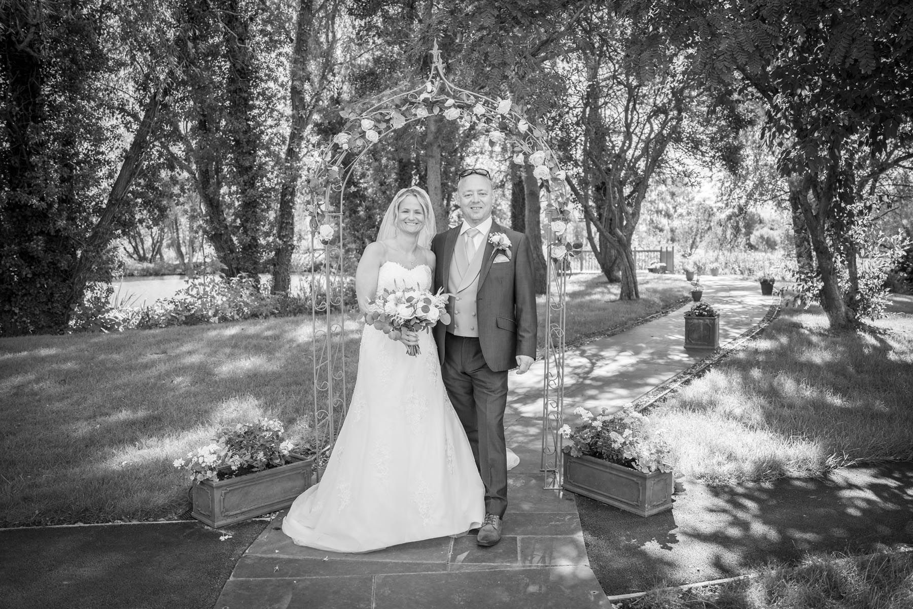 A black and white photo of a bride and groom standing next to each other in a park.