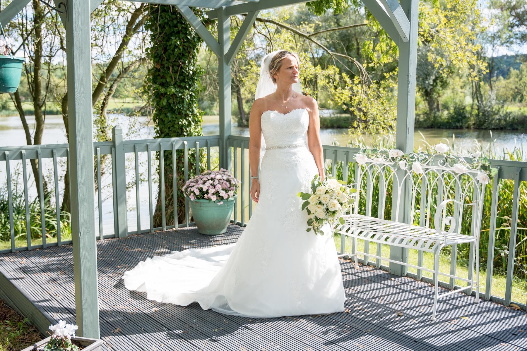 A bride in a wedding dress is standing under a gazebo holding a bouquet of flowers.