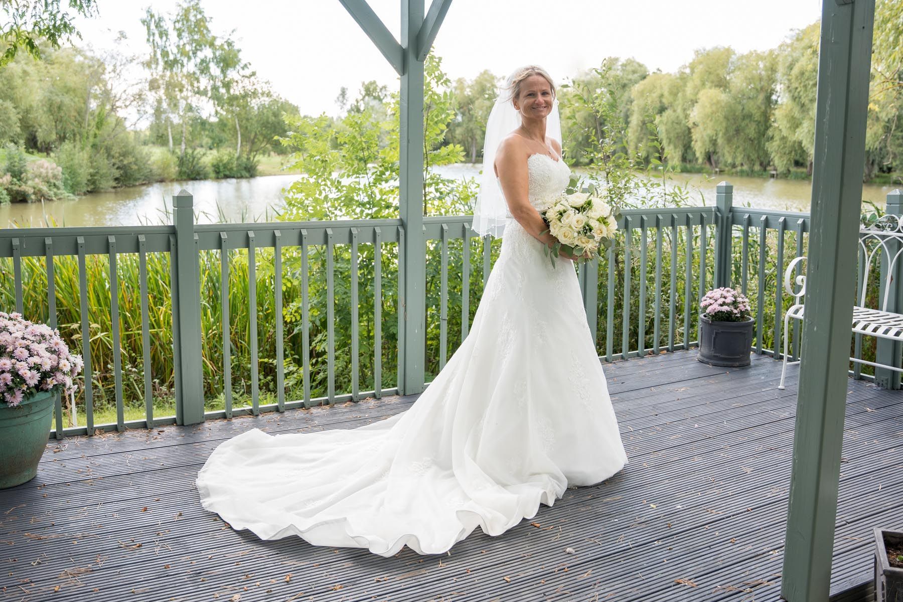 A bride in a wedding dress is standing on a deck holding a bouquet of flowers.
