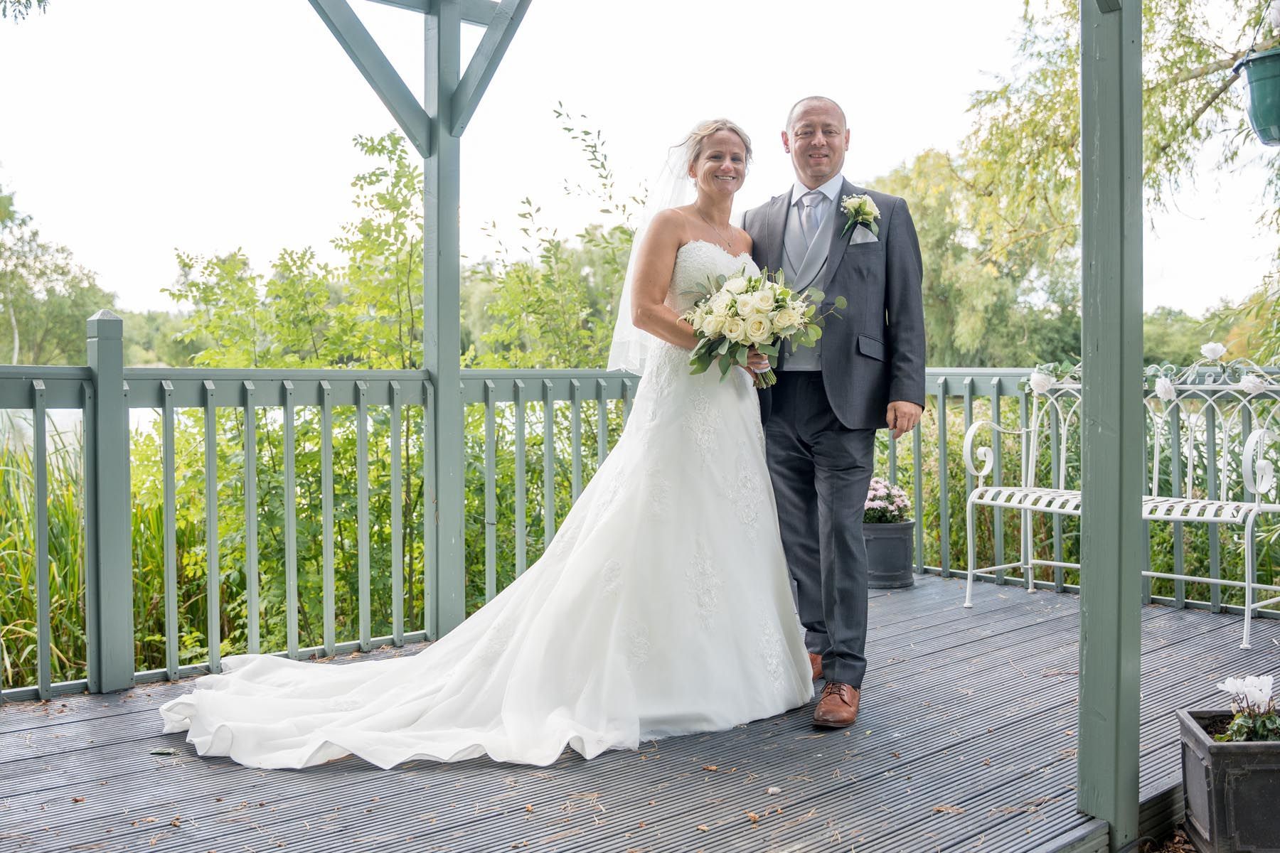A bride and groom are posing for a picture on a deck.