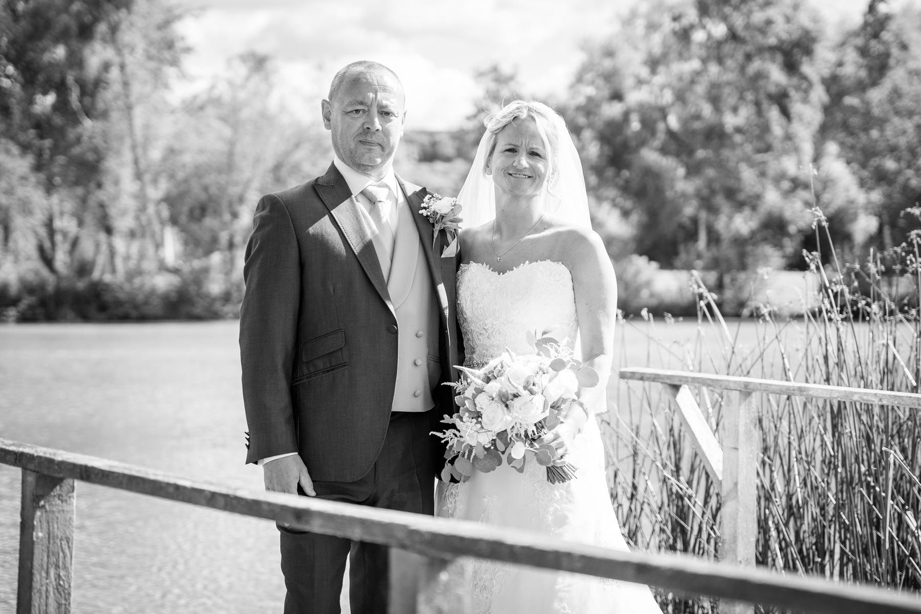 A black and white photo of a bride and groom standing on a bridge.