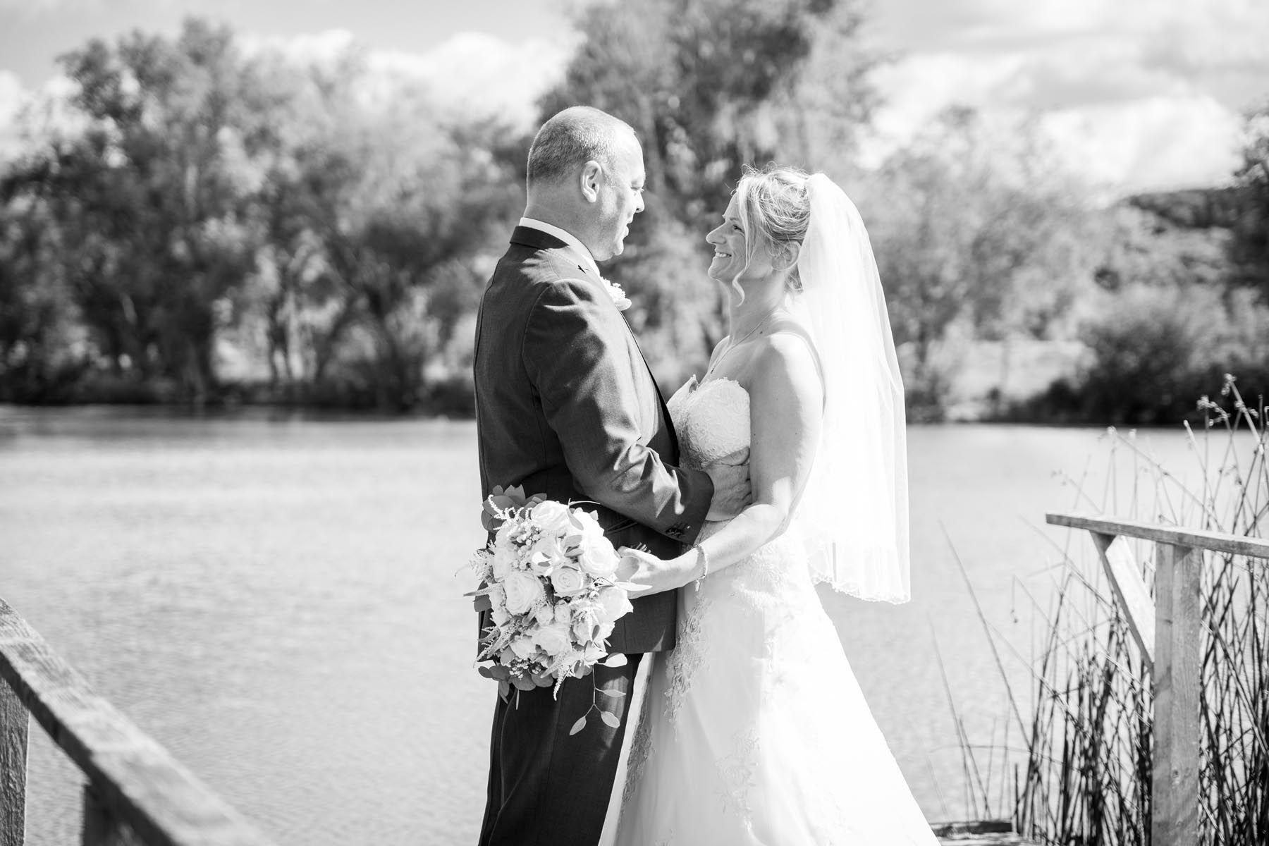 A bride and groom are standing on a bridge overlooking a lake.