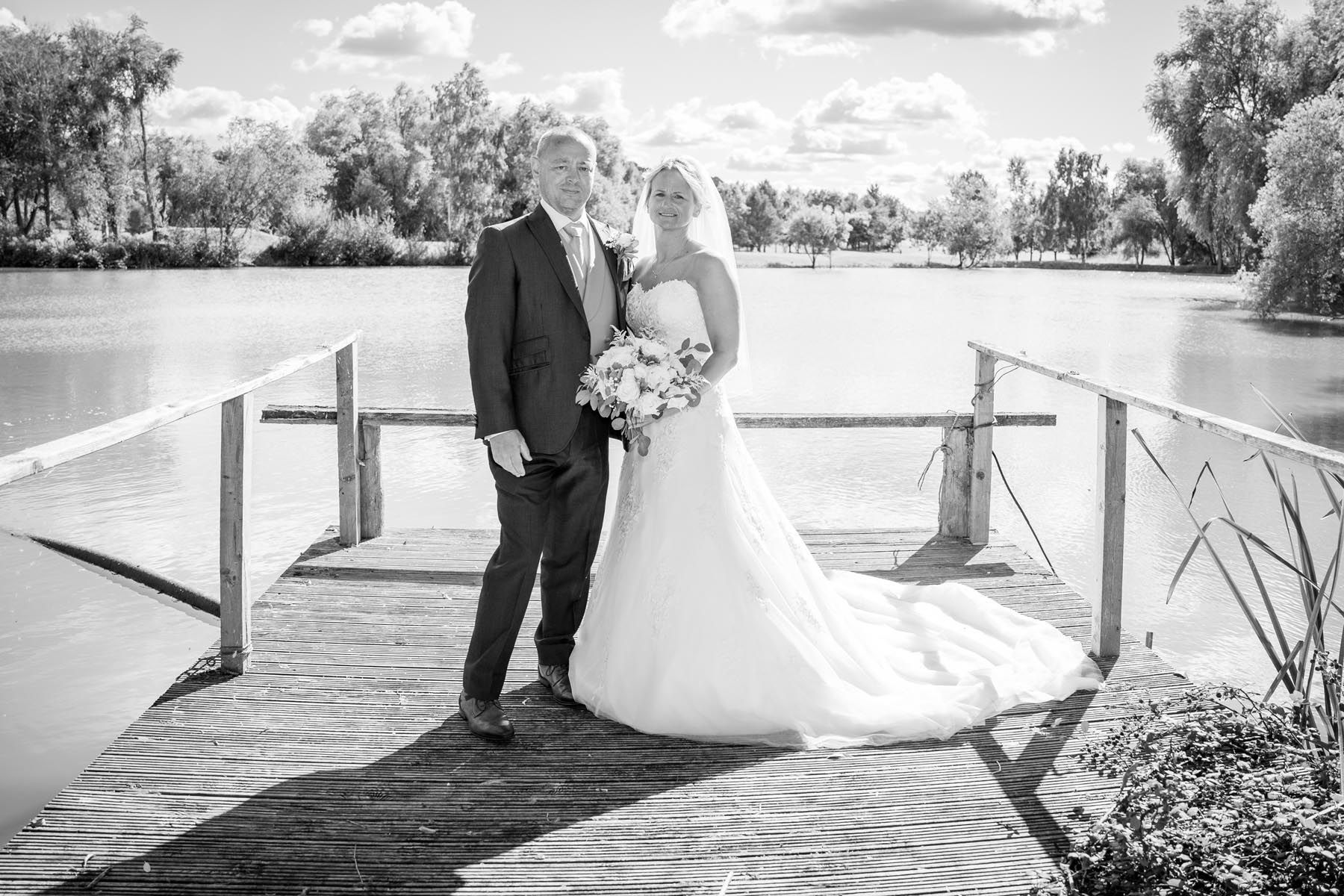 A black and white photo of a bride and groom standing on a dock.