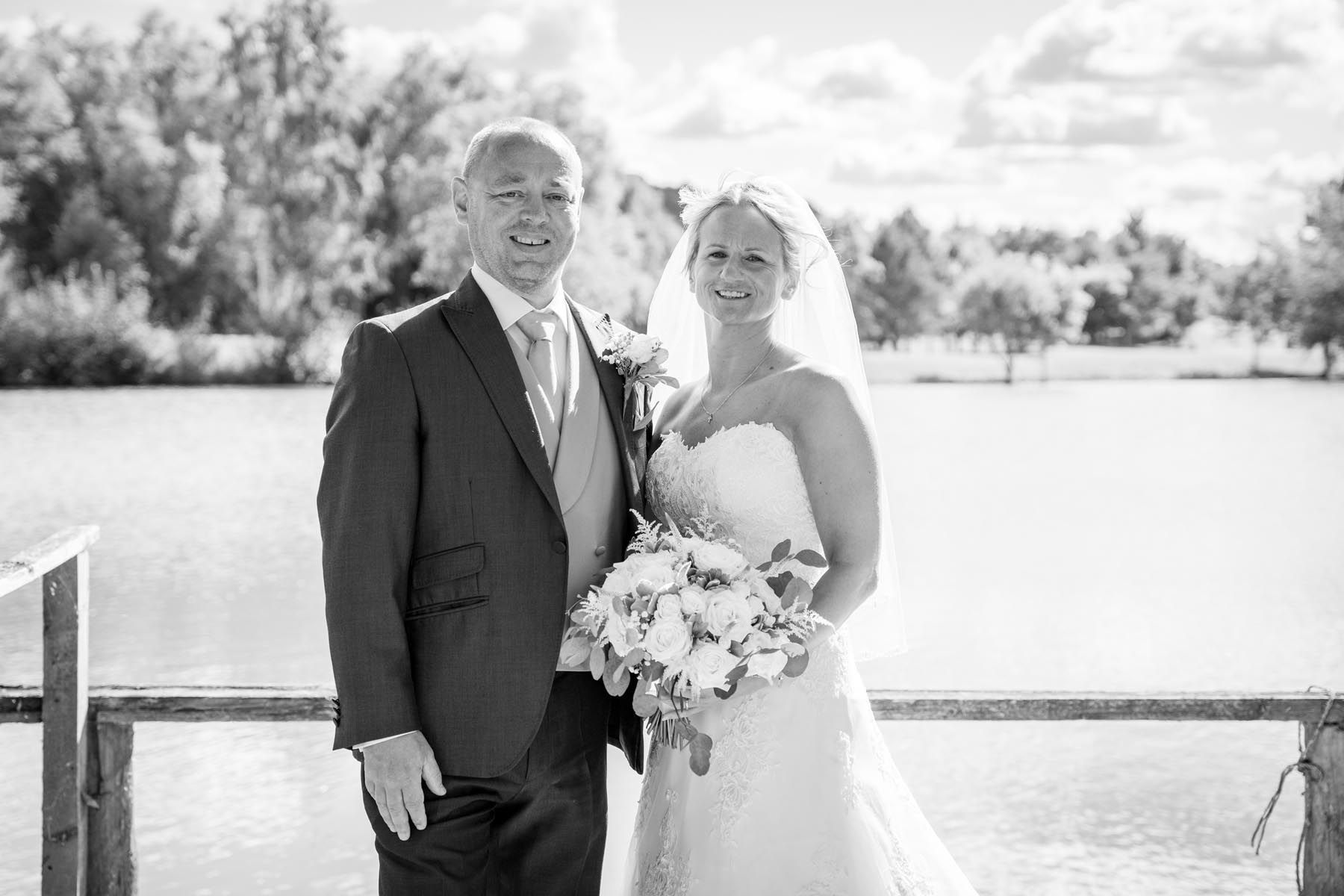A bride and groom are posing for a black and white photo on a dock.