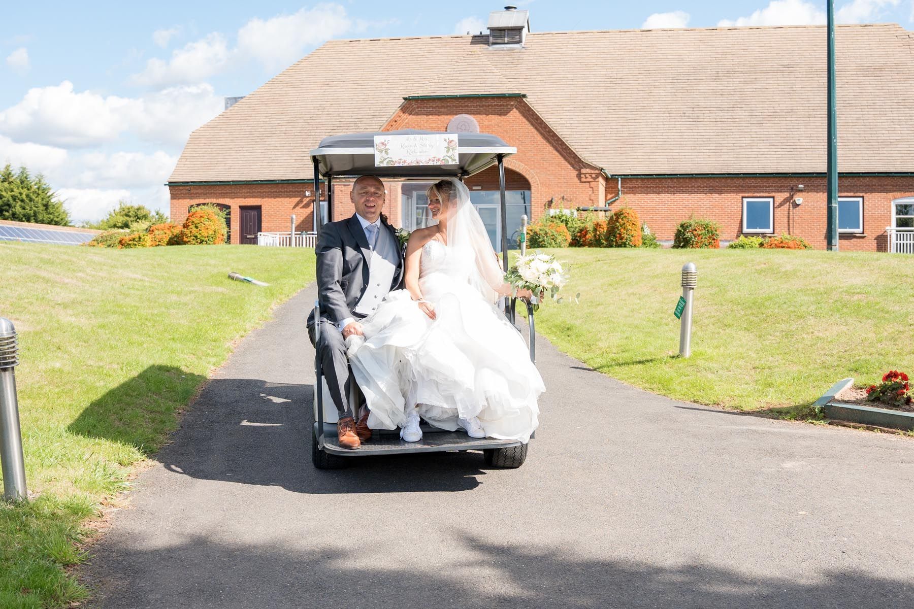 A bride and groom are riding in a golf cart.
