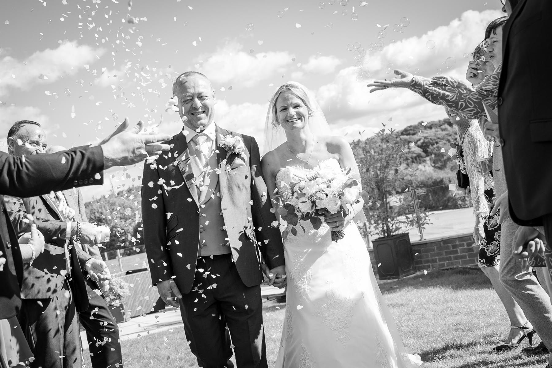 A black and white photo of a bride and groom being showered with confetti.