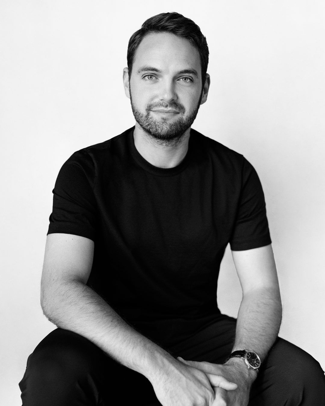 Black and white portrait of Sam Thomas, seated, in a black T-shirt.