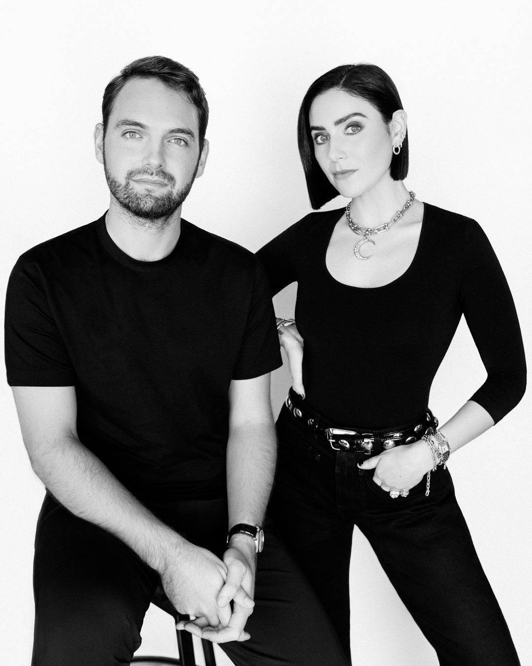 Black and white portrait of Sam Thomas and Lindy Firstenberg, both dressed in black against a white background.
