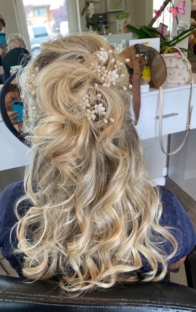 Blonde half-up curly hairstyle with jeweled floral hair accessory at a salon seating area