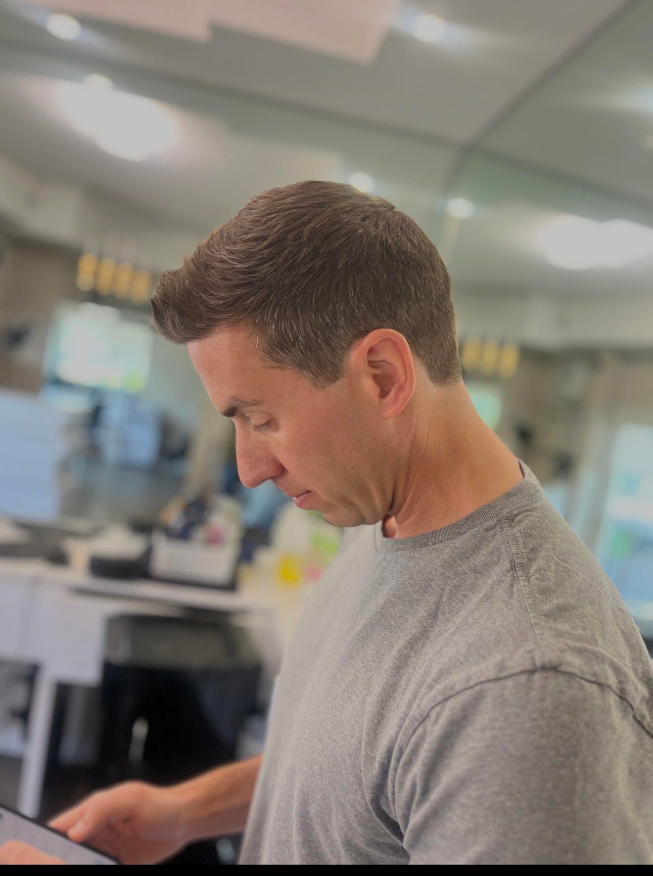 Man in gray shirt looking down at a tablet in a bright office setting