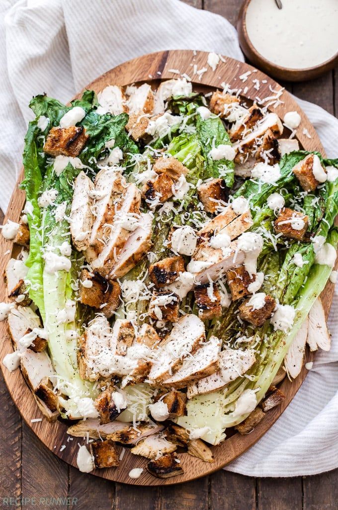 A caesar salad with chicken and lettuce on a wooden cutting board.