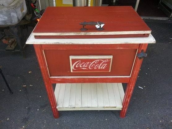 Red Coca-Cola cooler on a wooden stand with a white shelf underneath