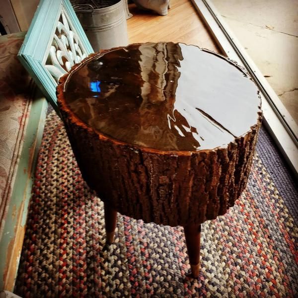 Rustic tree-stump side table with a glossy dark top on a woven rug near a framed mirror.