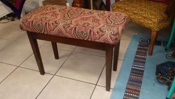 Patterned upholstered bench with wooden legs on a tiled floor beside a blue rug and chair