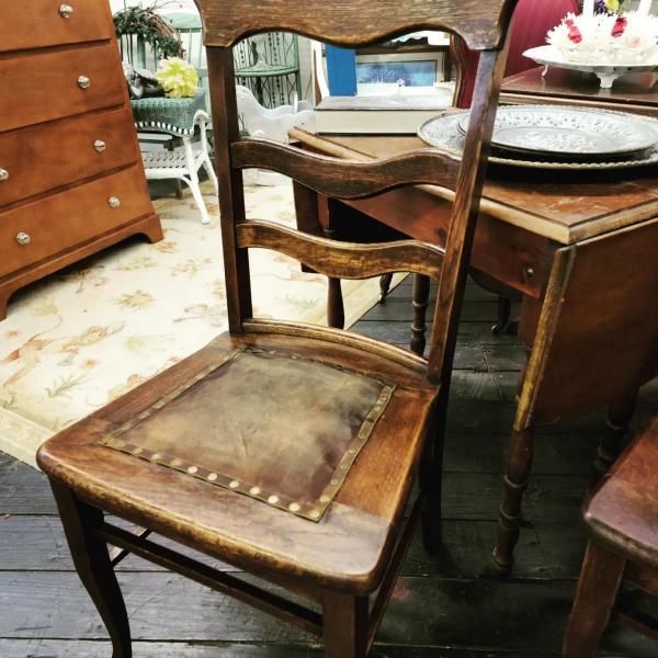 Wooden dining chair with a worn brown leather seat beside a wooden table in an antique store