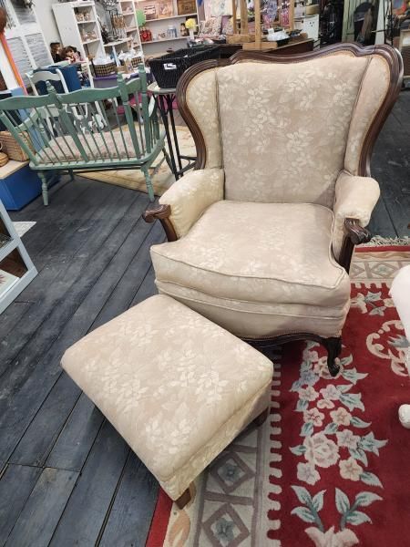 Beige upholstered armchair with matching ottoman in a thrift store aisle